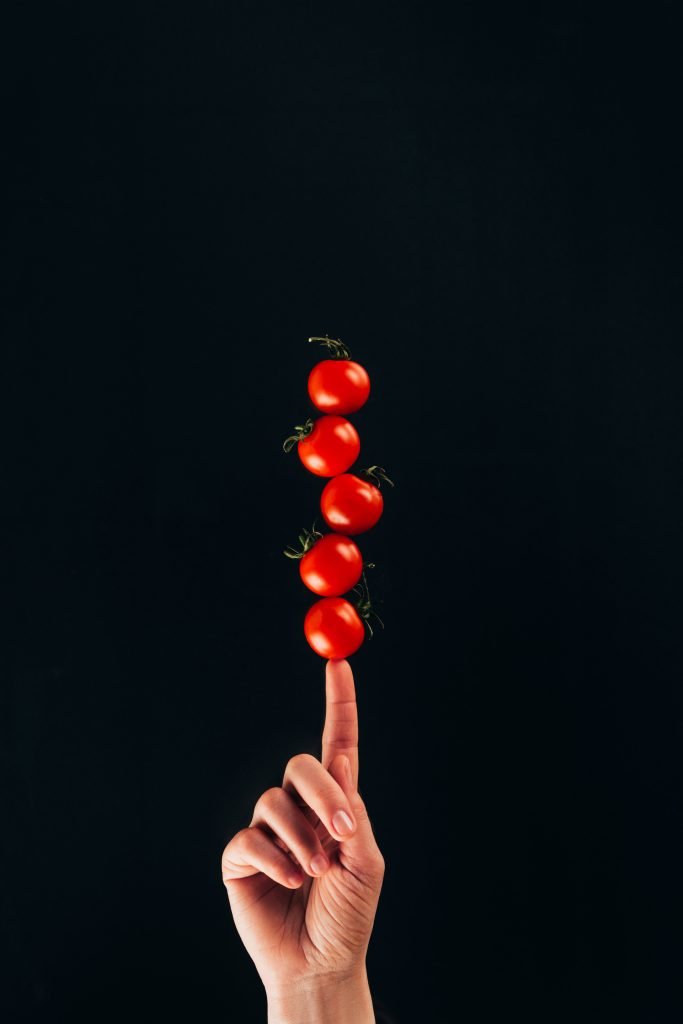 cropped shot of woman holding cherry tomatoes on finger isolated on black
